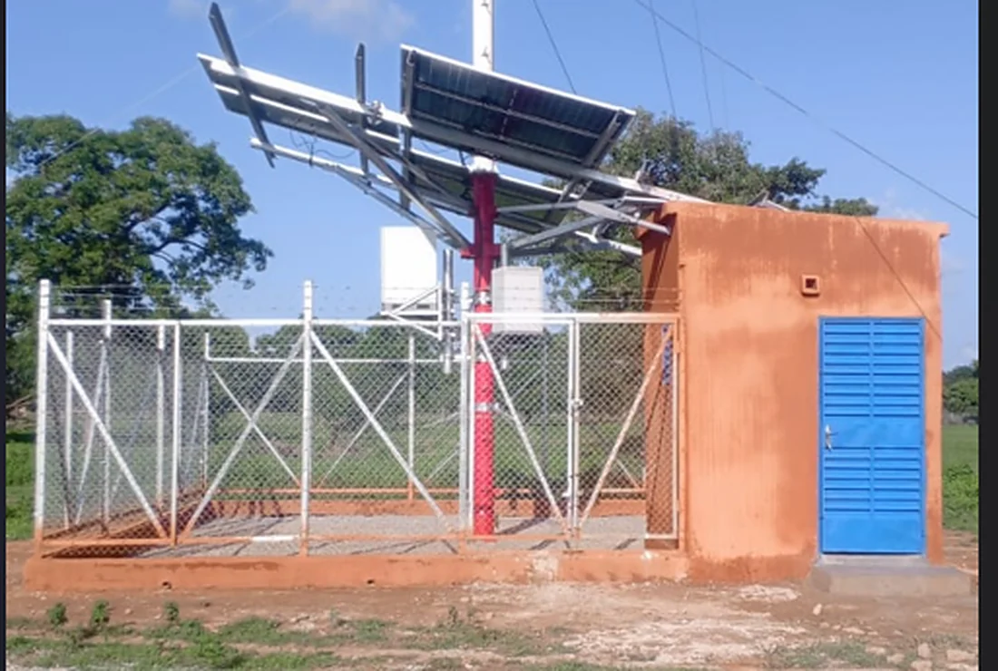 Site télécom rural clôturé avec guérite à porte bleue, pylône et panneaux solaires